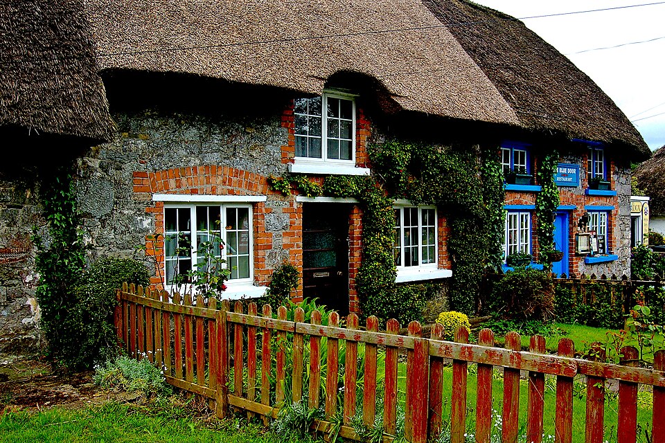 Thatched cottage with flower planting and a red timber fence.