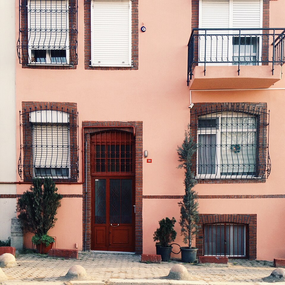 Red entrance door in a peach-colored facade with wrought-metal window grilles.