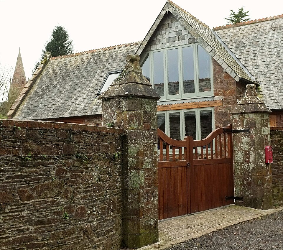 Timber entrance and glazing beneath a gabled stone coach house roof.