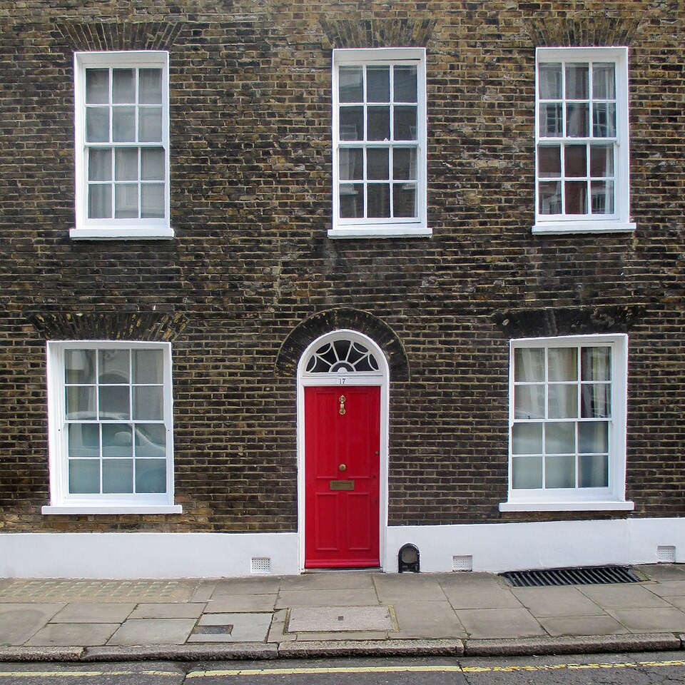 Red door with a white arched surround on a brick townhouse facade.