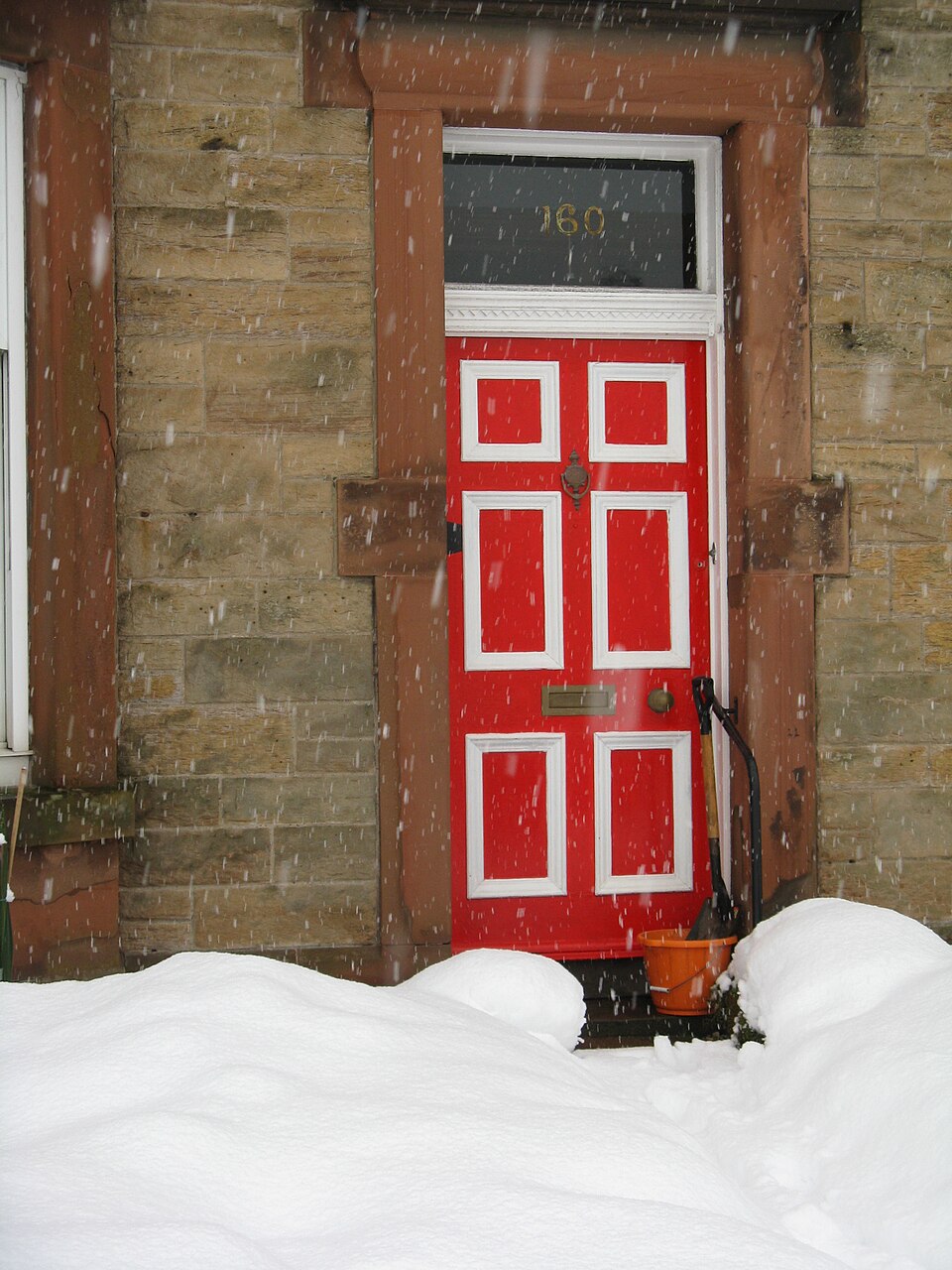 Red paneled entrance door beside a snow bank.