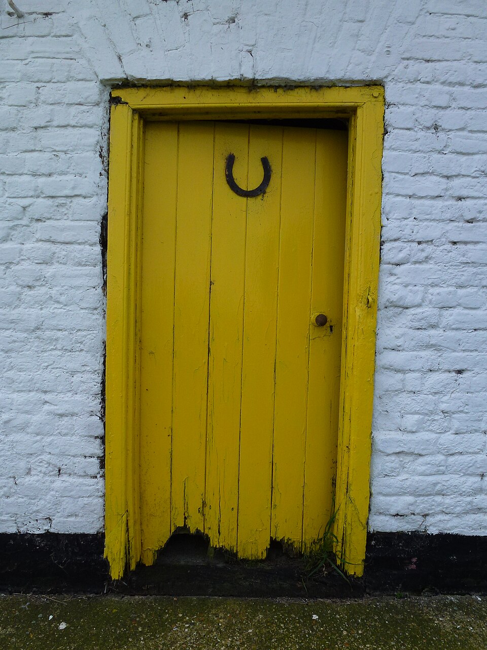 Yellow plank cottage door with a dark horseshoe ornament.