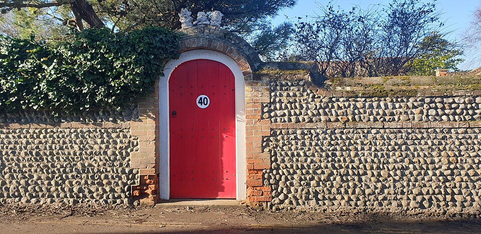 Rounded red door in a flint wall in Mundesley, England.