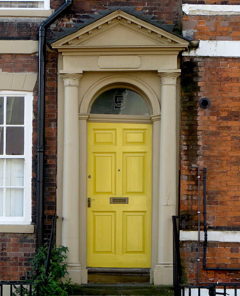 Yellow paneled door framed by an elaborate classical surround.