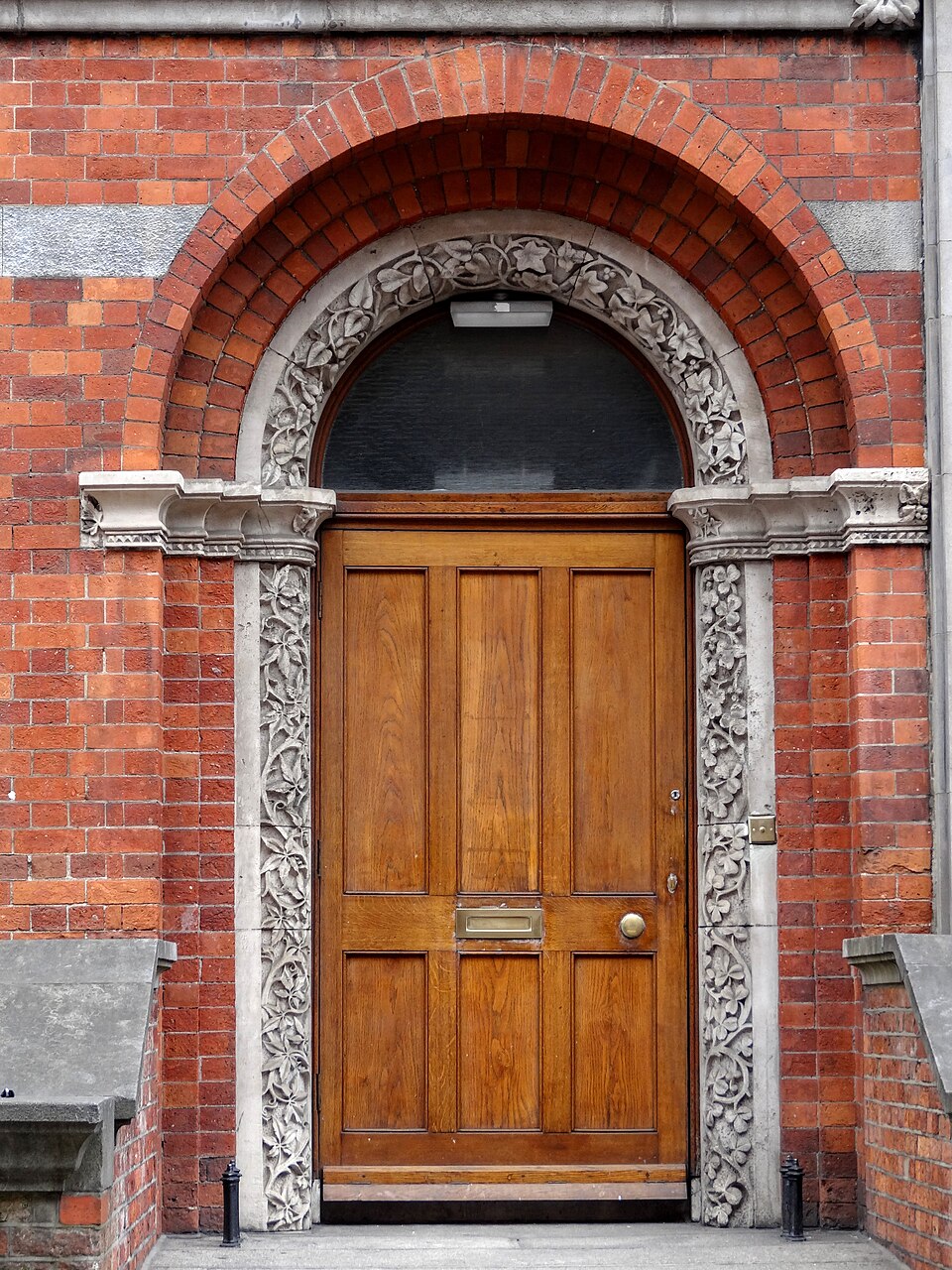 Natural-wood double doors with a fanlight in a brick arch in Dublin.