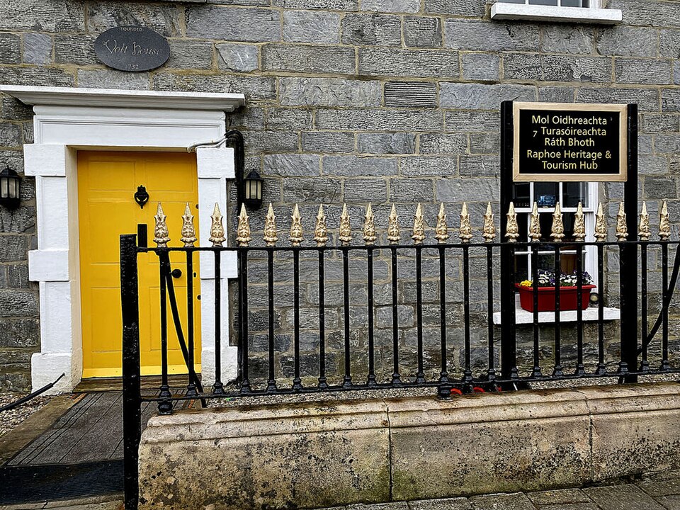 Yellow door set within a pale facade and black iron railings.