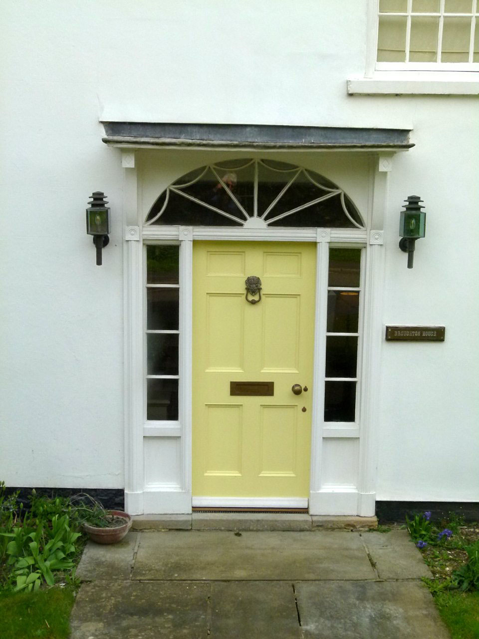 Pale yellow entrance with sidelights, fanlight, and paired wall lanterns.