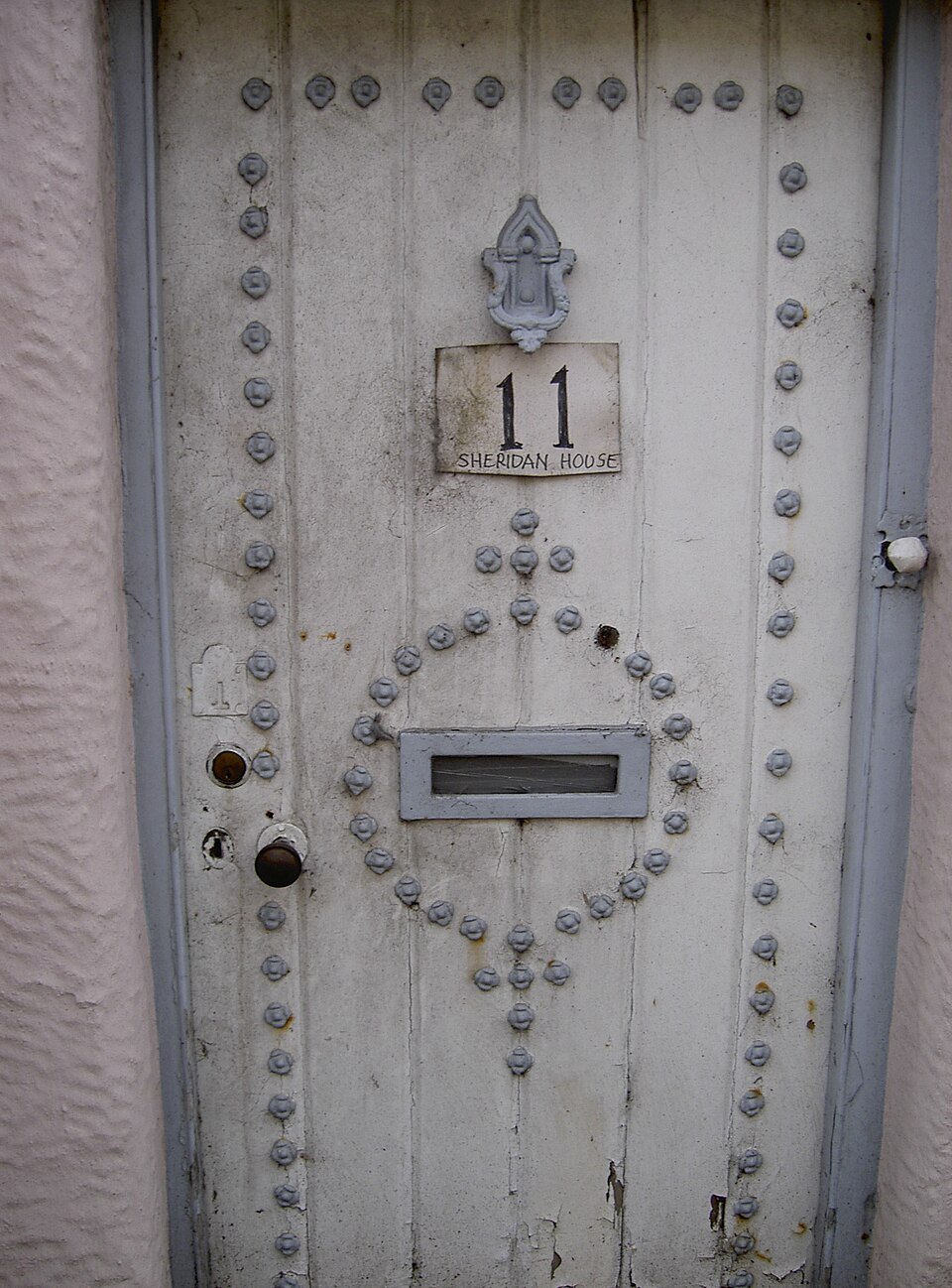 Pale painted door with ornamental metalwork and a glazed upper panel.