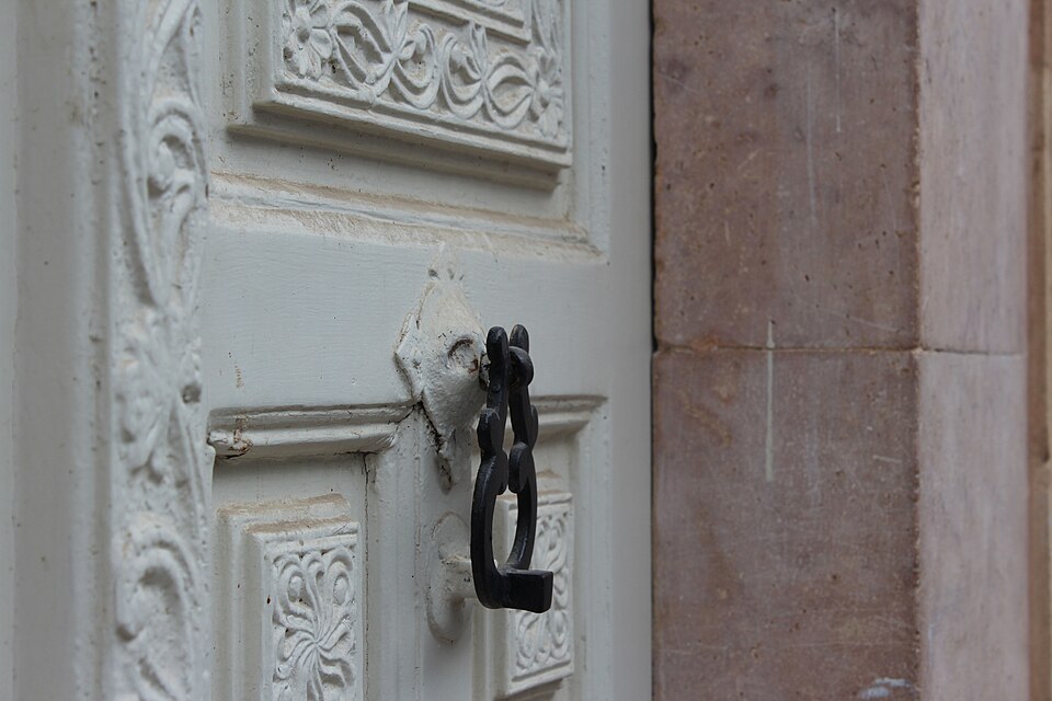 Close view of a white carved wooden door and dark metal knocker.