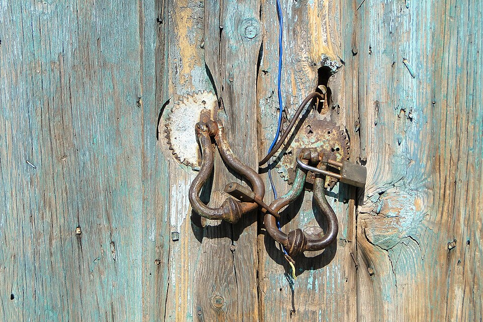 Old iron locks and knockers on a weathered turquoise timber door in Ayvalik, Turkey.