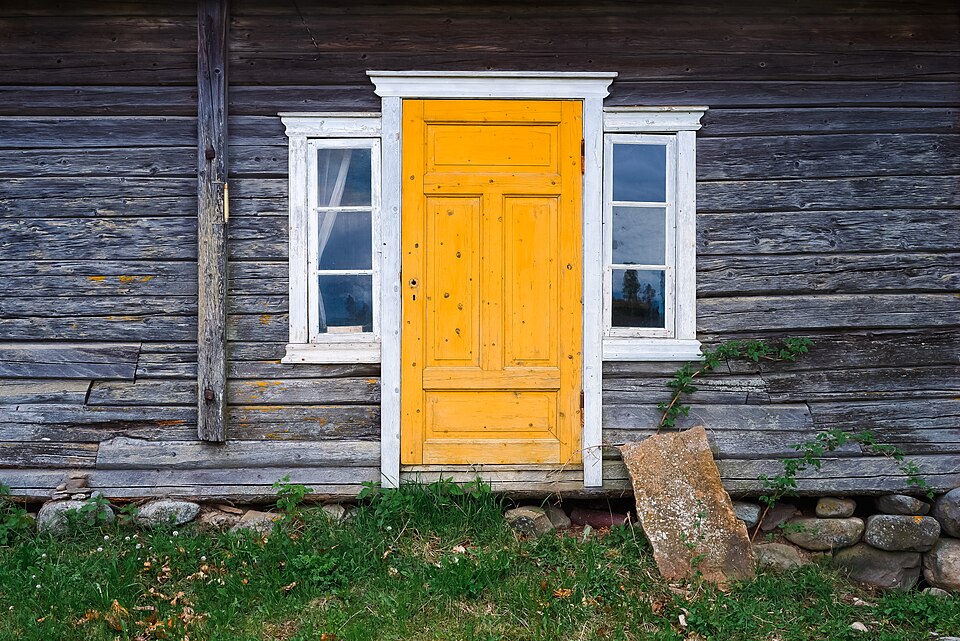 Yellow door and white sidelights in a weathered timber wall.